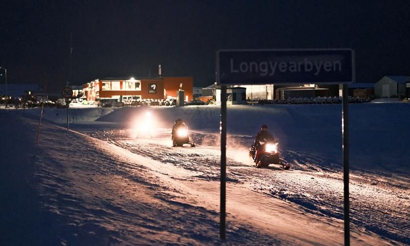 Snøscootere på vei ut av Longyearbyen med byskiltet i front