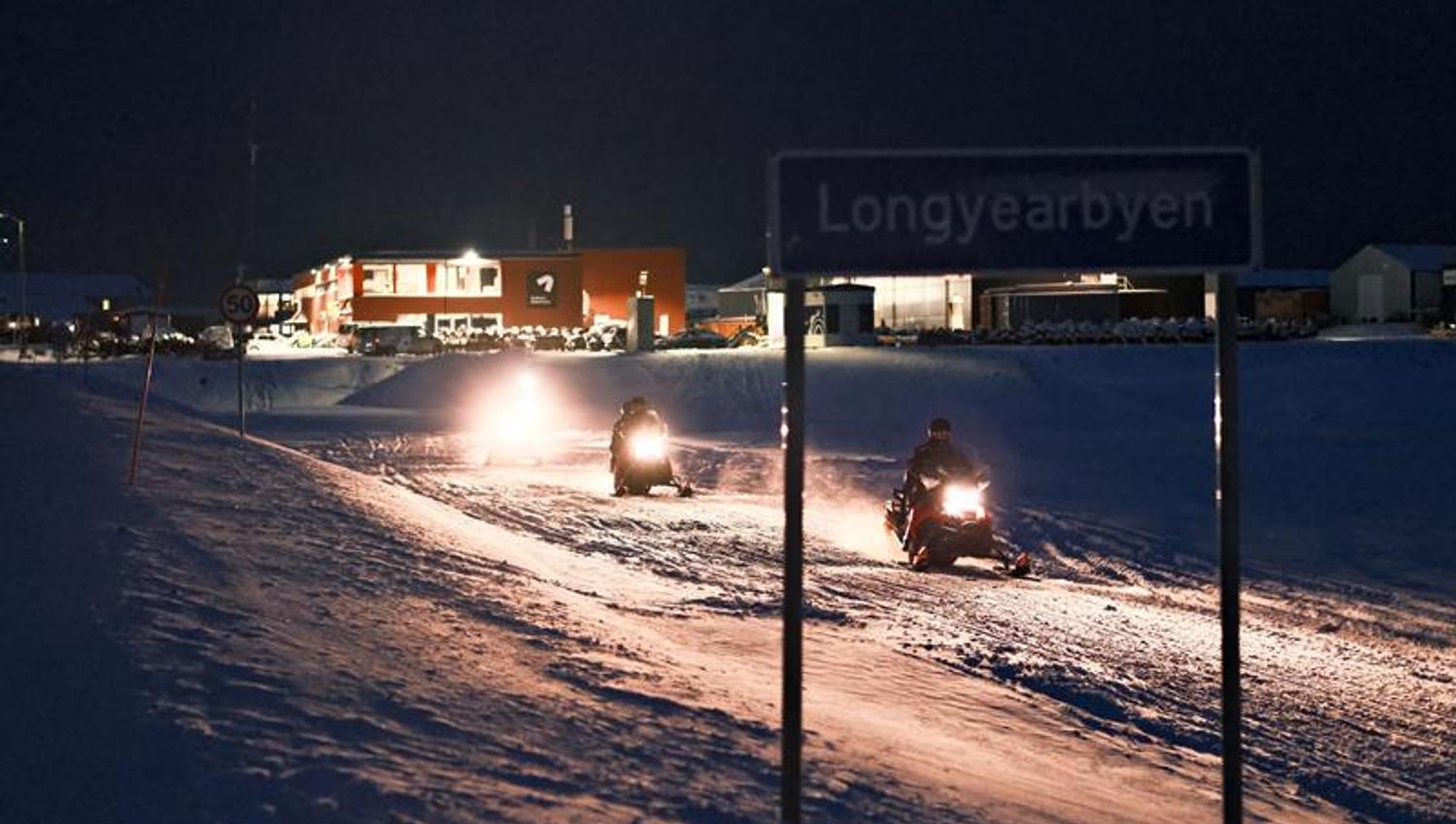 Snøscootere på vei ut av Longyearbyen med byskiltet i front