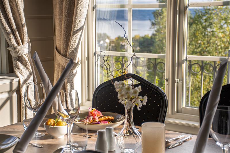 Set table with a plate of meat. Empty chair, sea view through the window behind