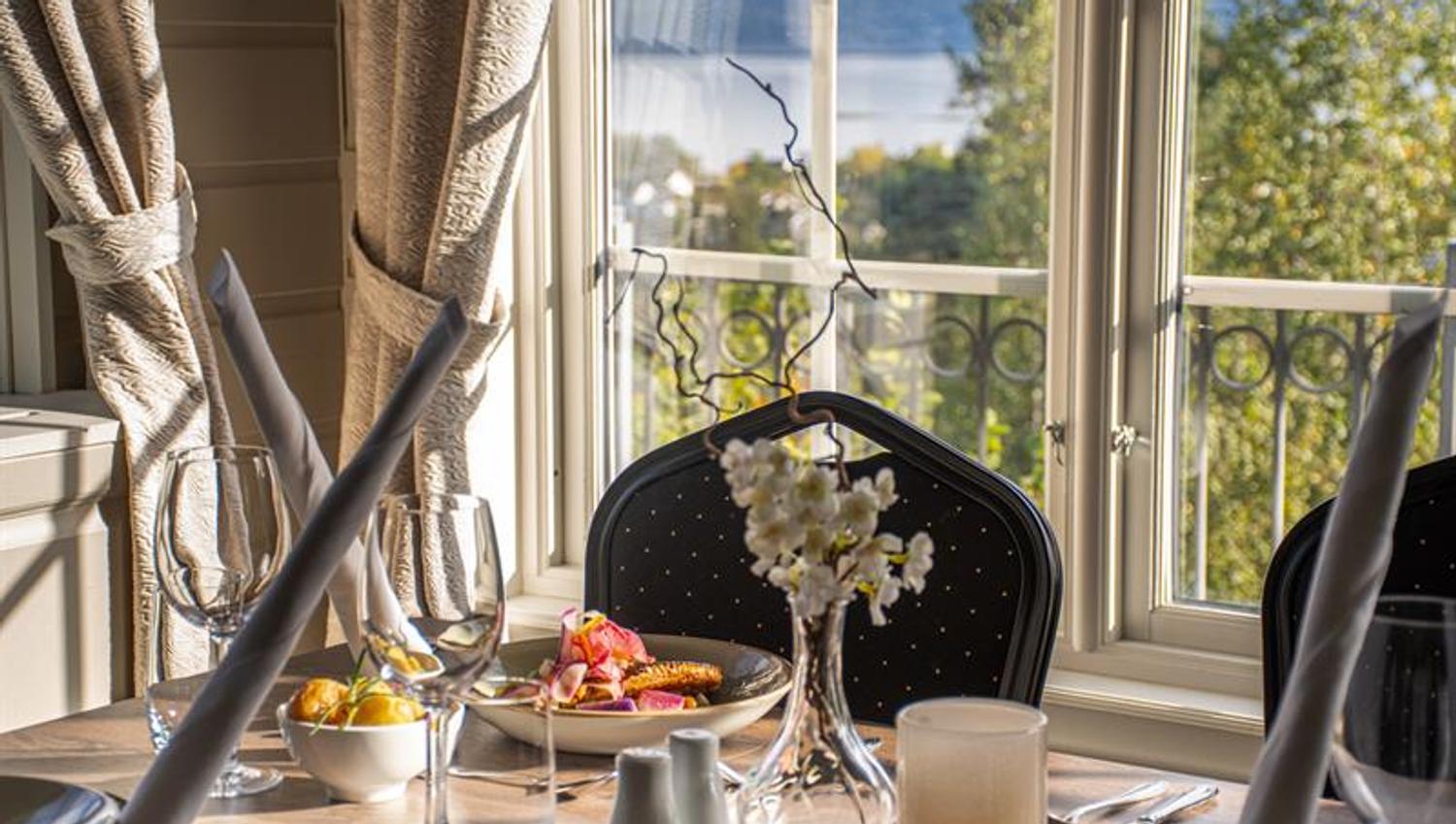 Set table with a plate of meat. Empty chair, sea view through the window behind