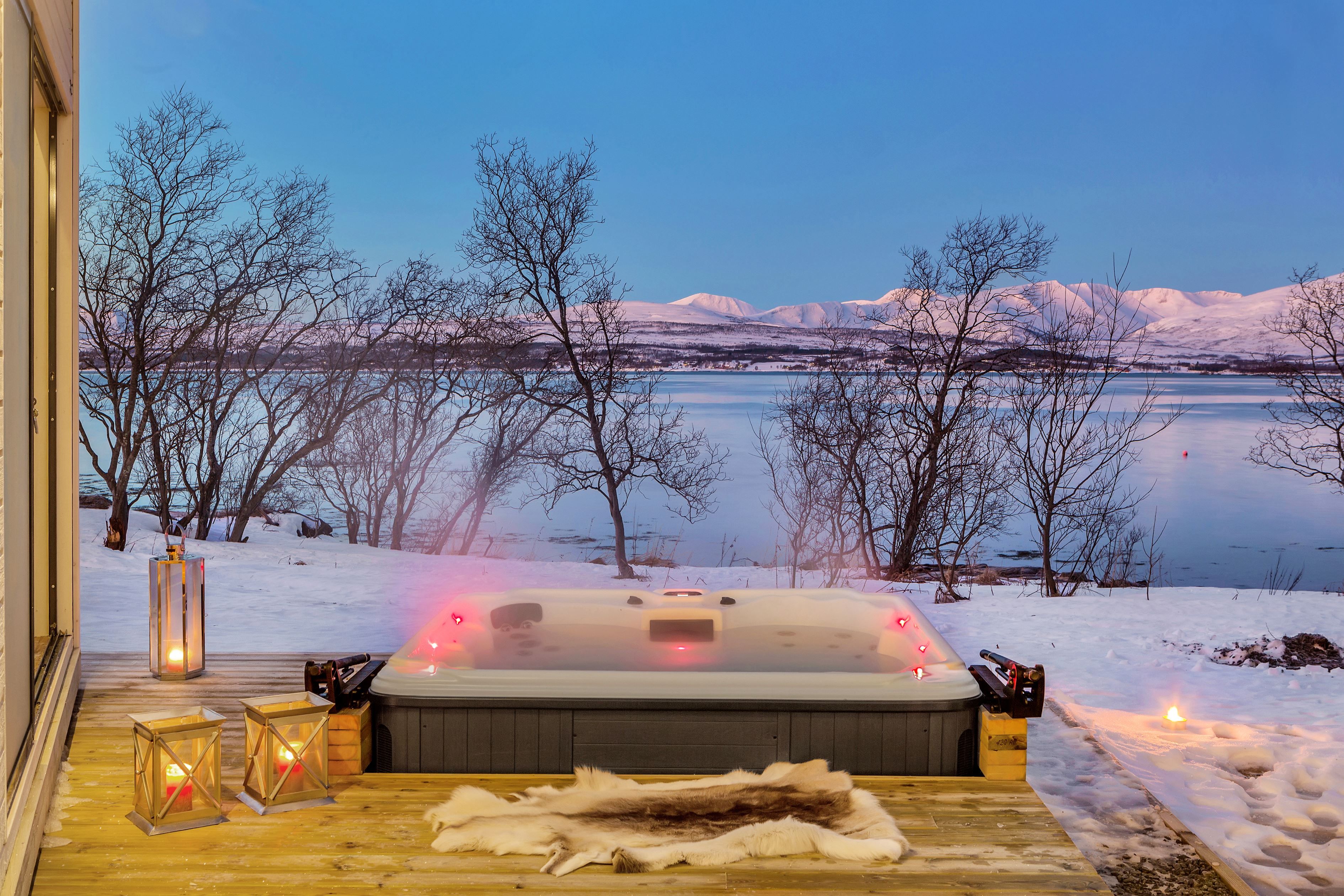 Utebadestamp på treterrasse omgitt av snø, med utsikt mot vann og fjell.