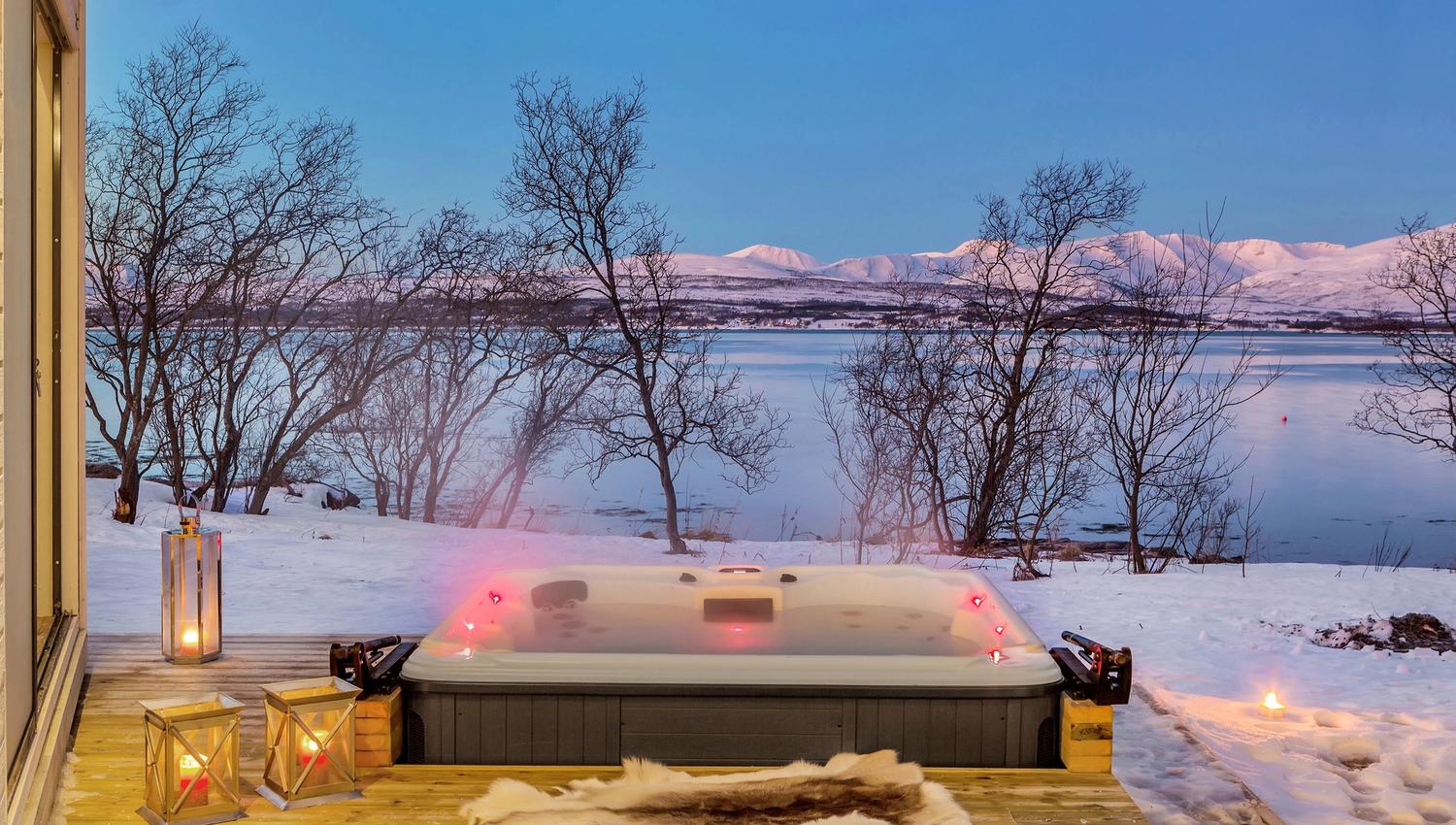 Utebadestamp på treterrasse omgitt av snø, med utsikt mot vann og fjell.