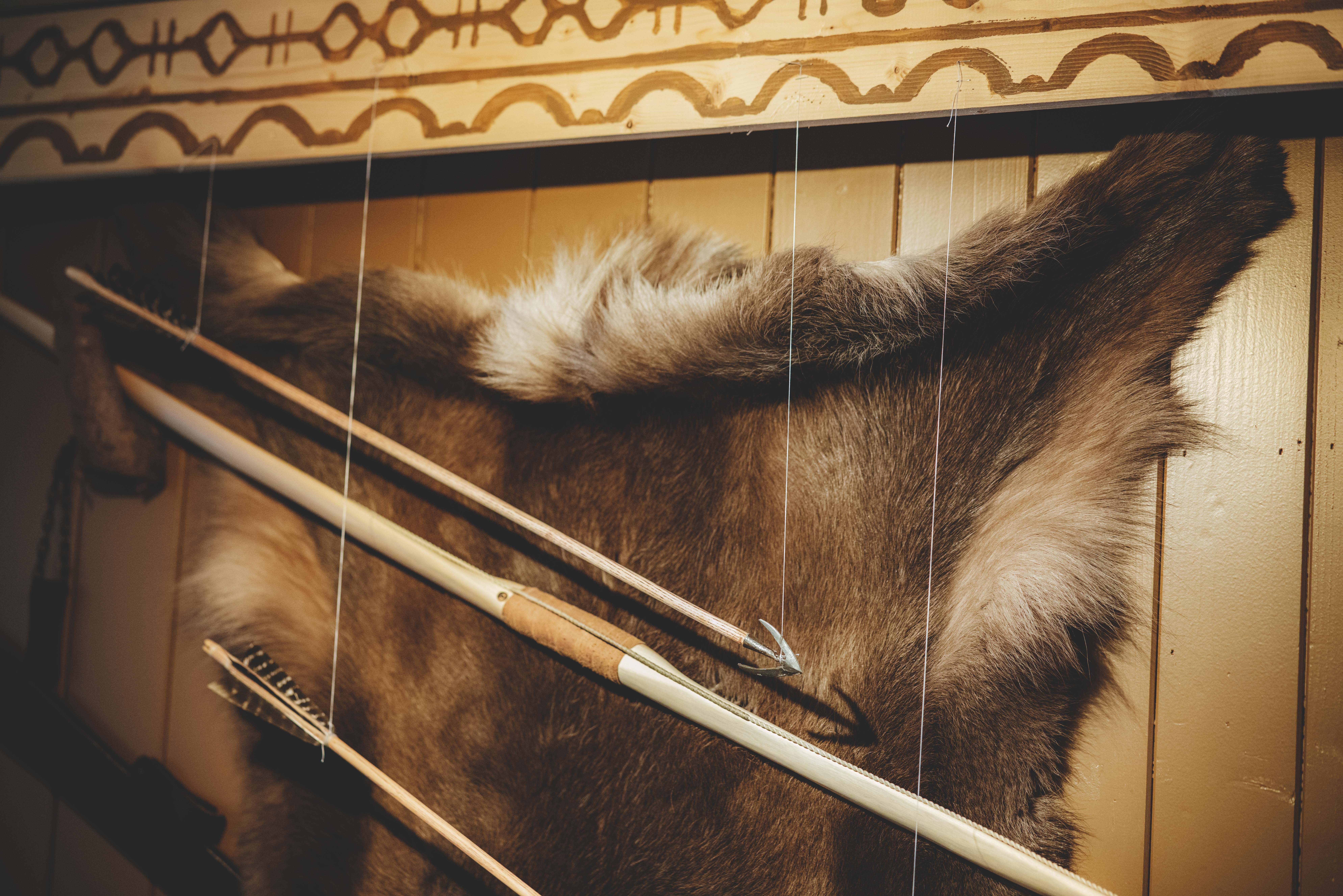 An der Wand ist ein Rentierfell befestigt, vor dem Fell befinden sich mehrere Wikingerspeere.