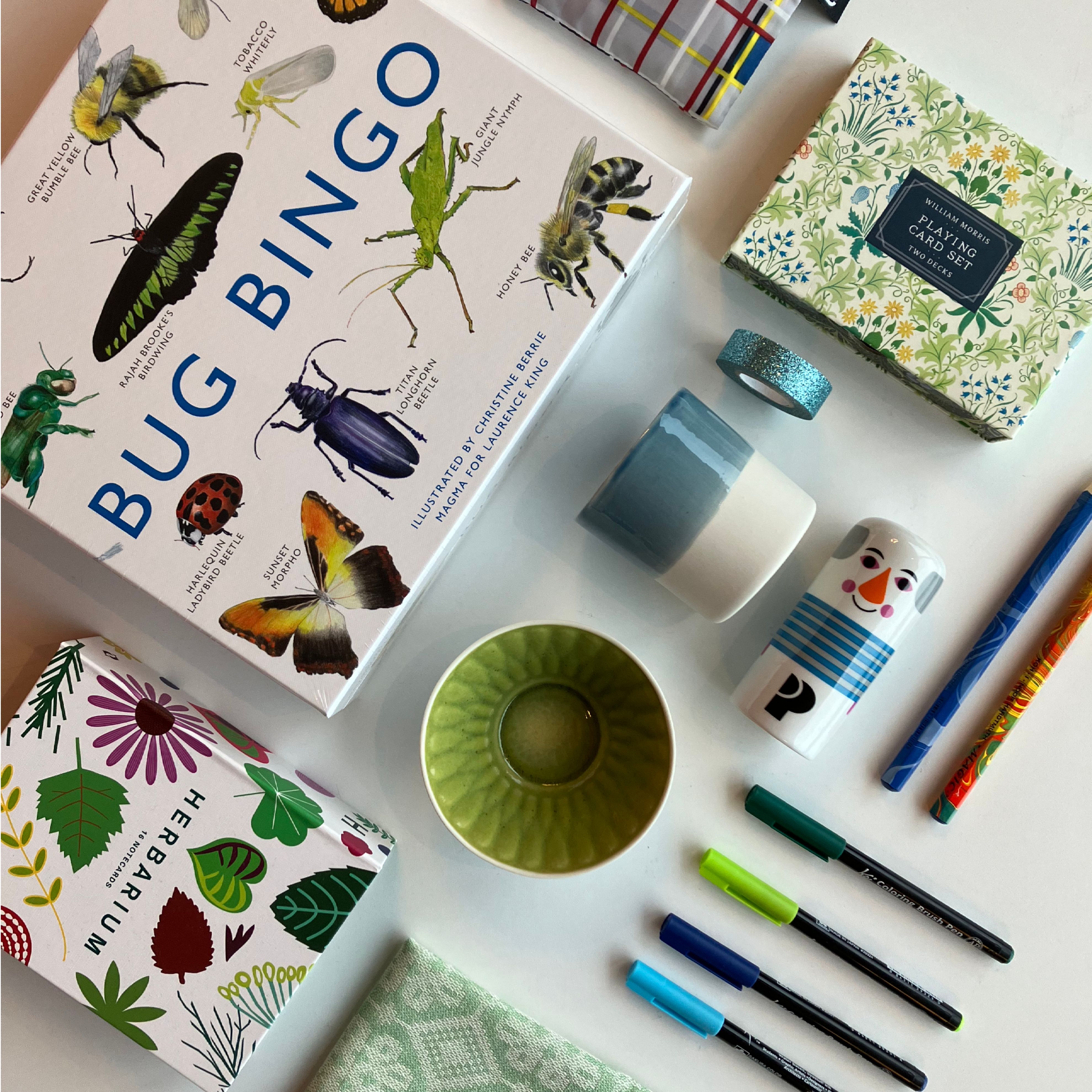 A selection of items from the museum shop: games, a deck of cards, colorful cups, markers, pencils, and small gift items displayed on a table.