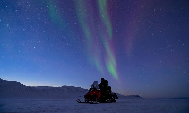 Snowmobile on snowcoveren landscape. Green and purple northern lights on the sky,