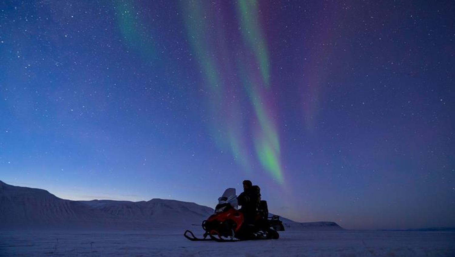 Snowmobile on snowcoveren landscape. Green and purple northern lights on the sky,