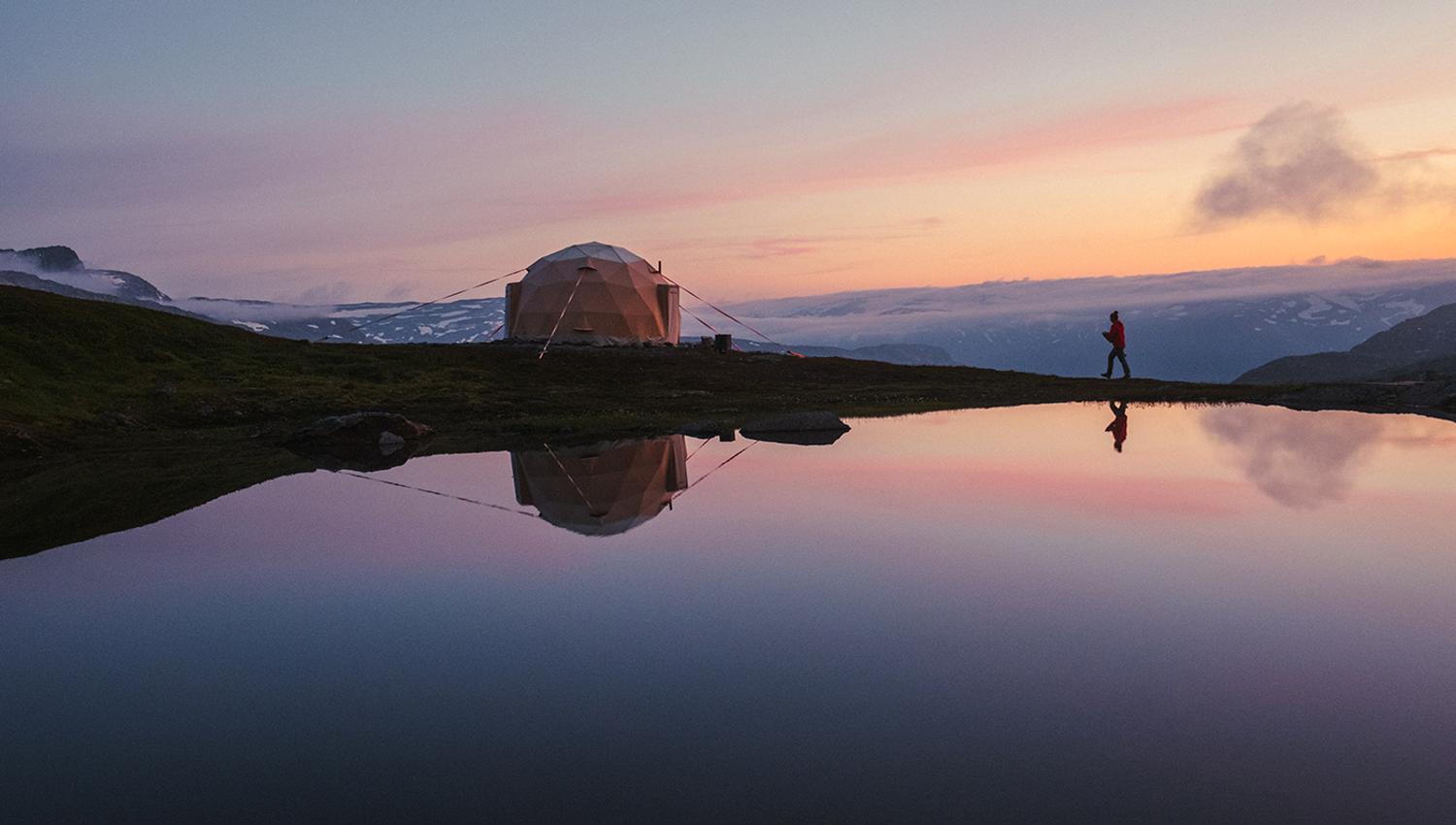 Geodesic glamping dome by a calm mountain lake at sunset near Trolltunga, Hardanger.