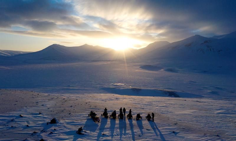 Gruppe mennesker står i solnedgang på snødekt vidde.