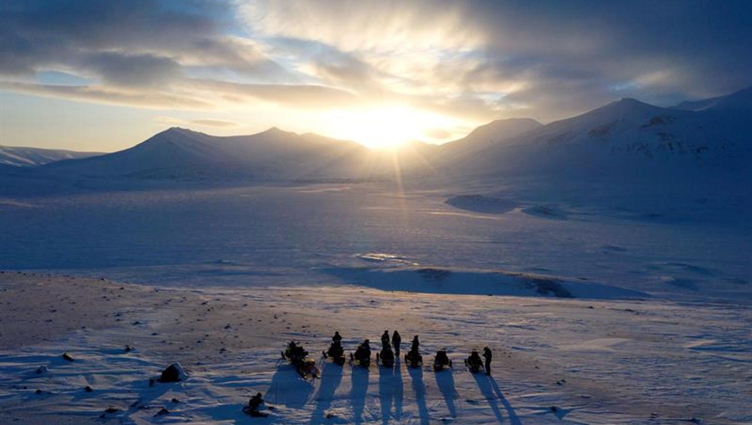 Gruppe mennesker står i solnedgang på snødekt vidde.