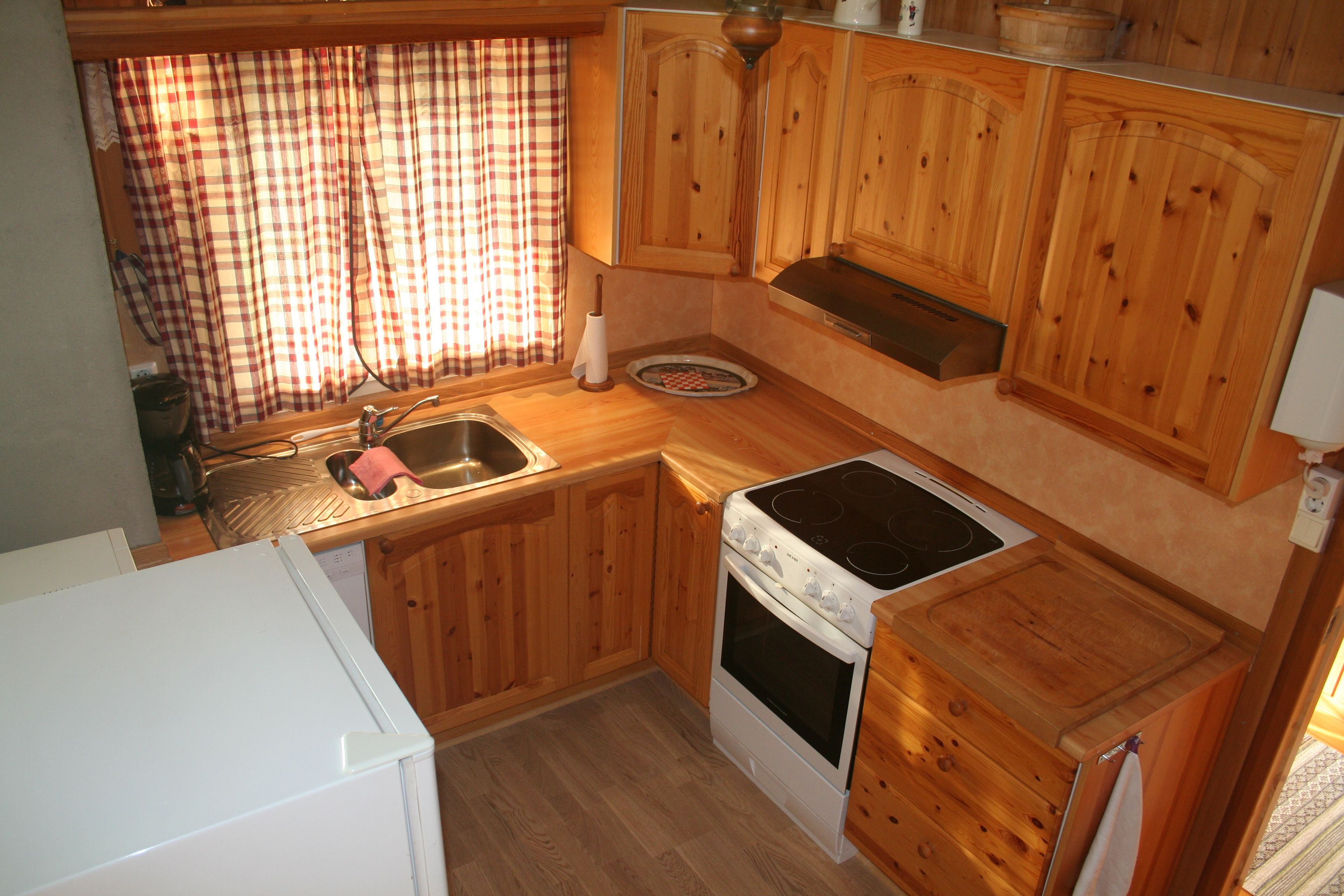 Cozy Norwegian cabin kitchen with wooden paneling, checkered curtains, and full amenities.