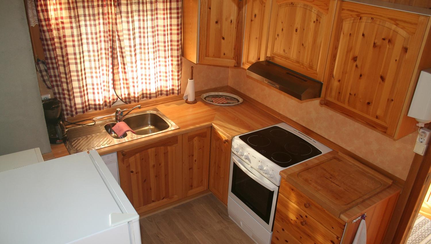 Cozy Norwegian cabin kitchen with wooden paneling, checkered curtains, and full amenities.