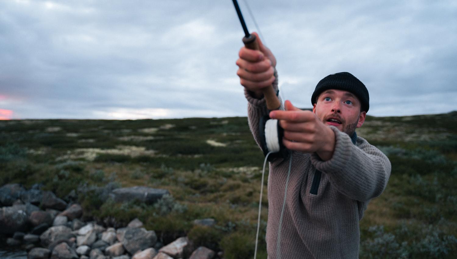 A close-up of a man throwing the line into a mountain lake.