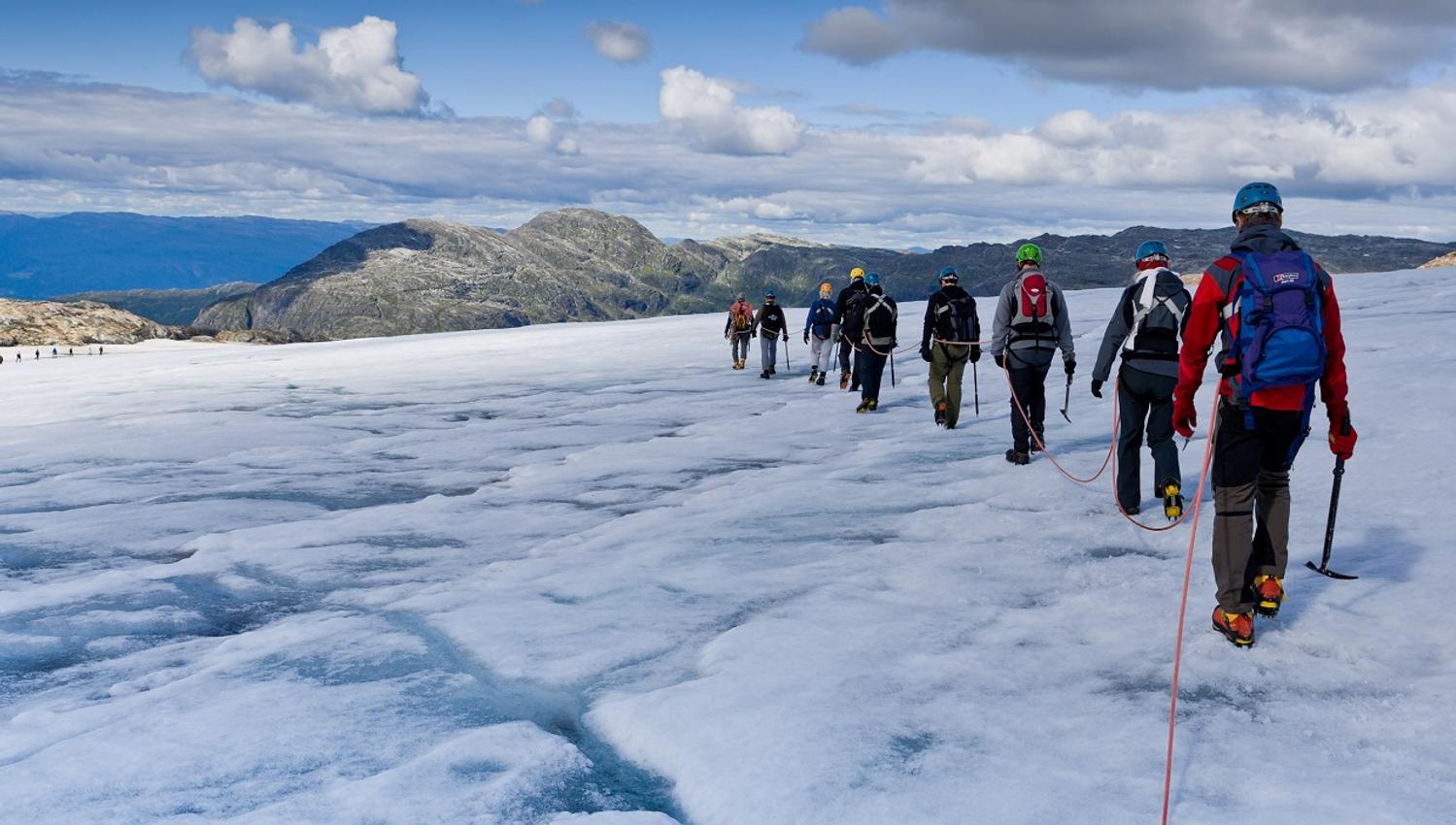 A group of hikers walking across the Folgefonna Glacier in Hardanger, led by a glacier guide with an ice axe and crampons.
