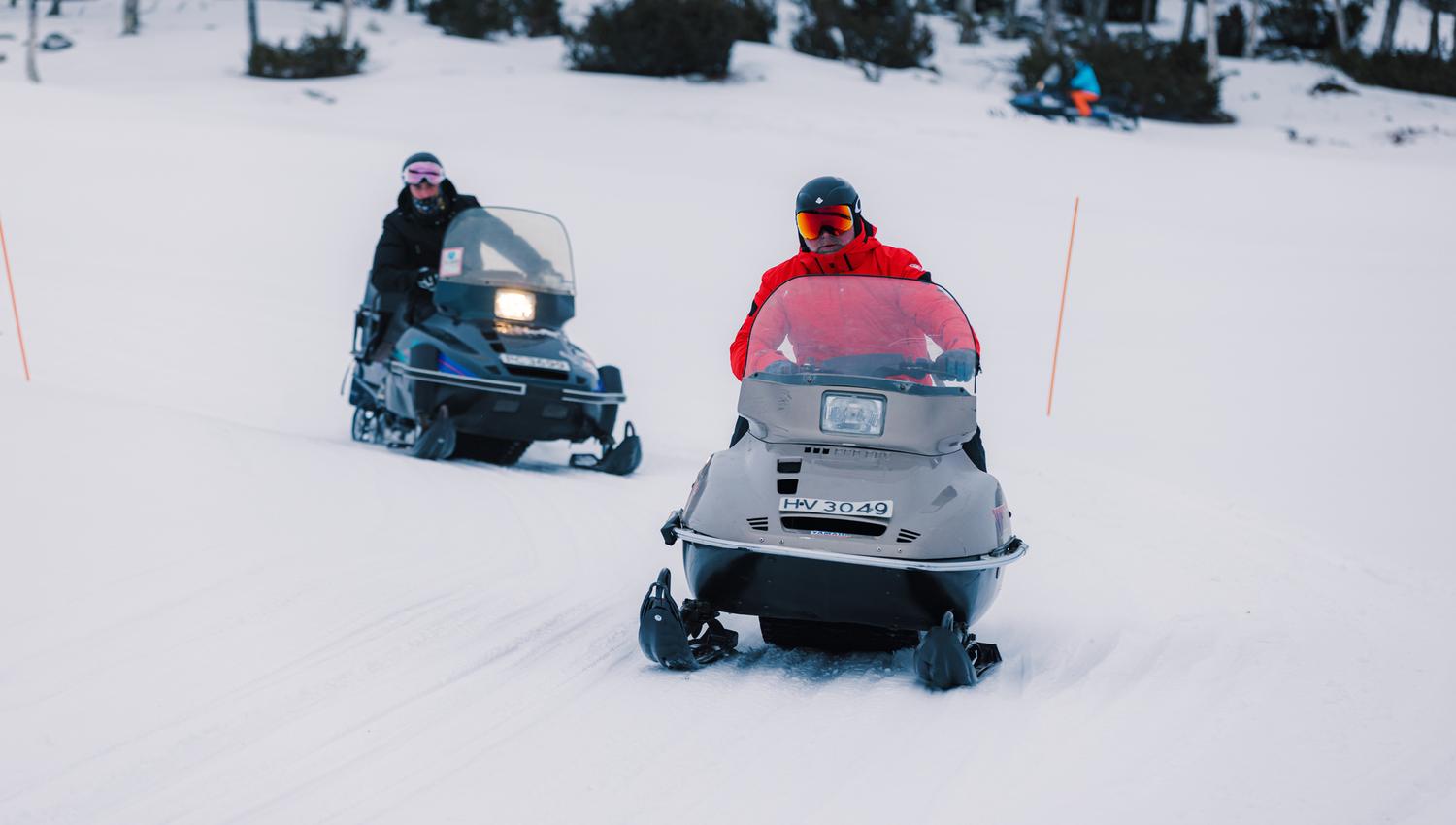 Two men on a snowmobile in a winter landscape.