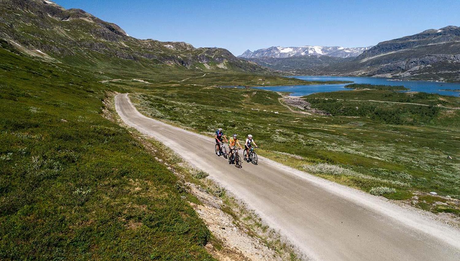 Cyclists on the climb on a gravel road to a mountain pass, with Jotunheimens high peaks in the background.