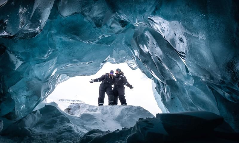 To personer står i åpningen av en isgrotte.