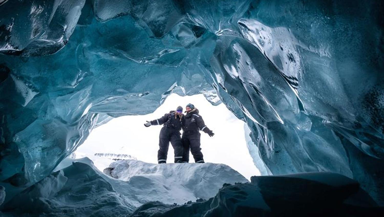 To personer står i åpningen av en isgrotte.