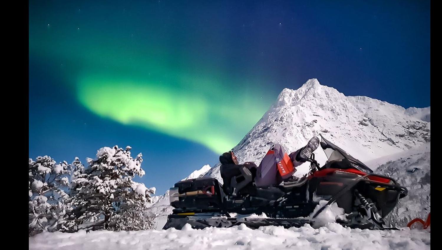 En person på snøskuter som ser opp på nordlyset