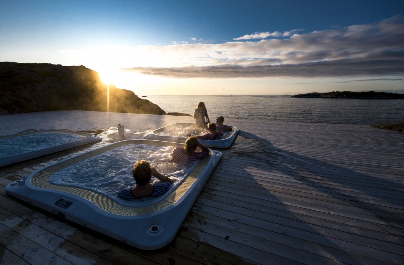 outdoor hot tub overlooking the fjord, with the midnight sun setting on the horizon