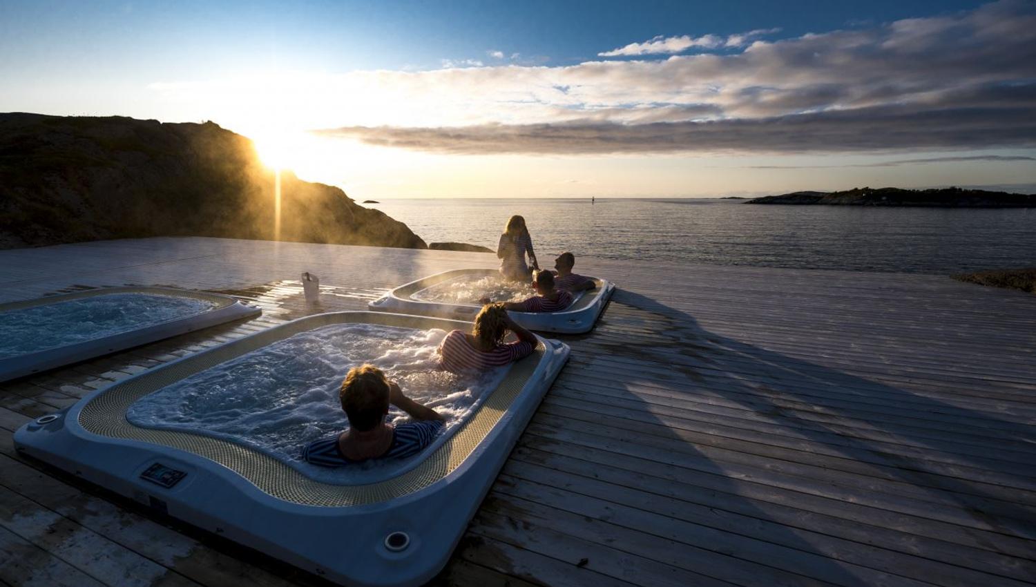 outdoor hot tub overlooking the fjord, with the midnight sun setting on the horizon