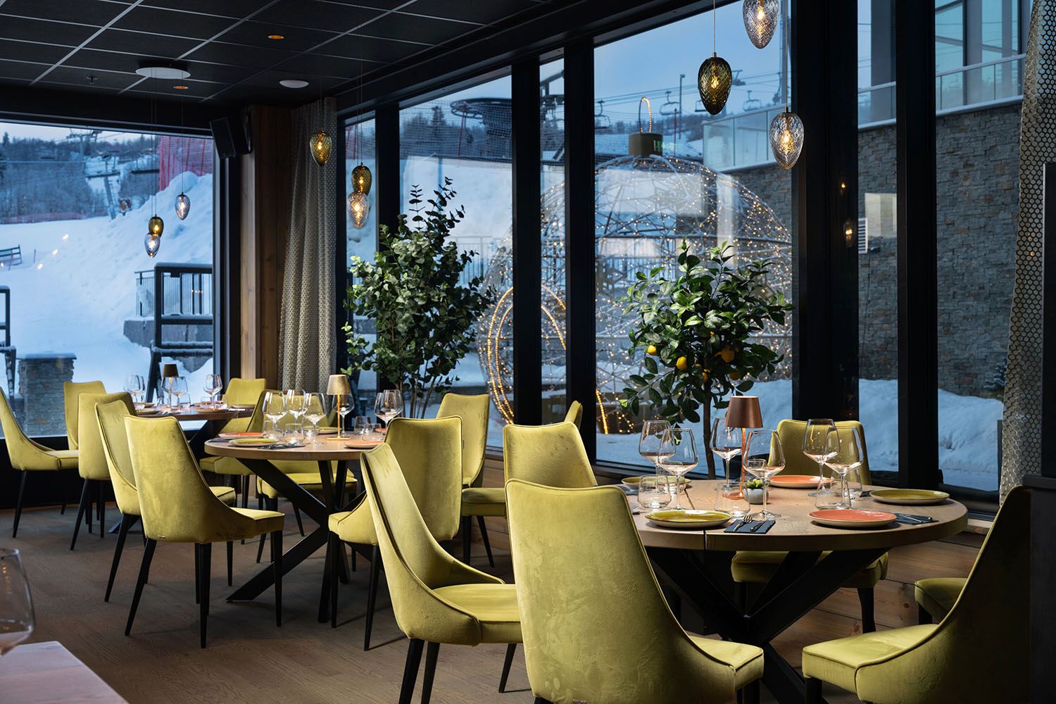 Restaurant interiour with light green cushion chairs and warm lightning. Snow outside.
