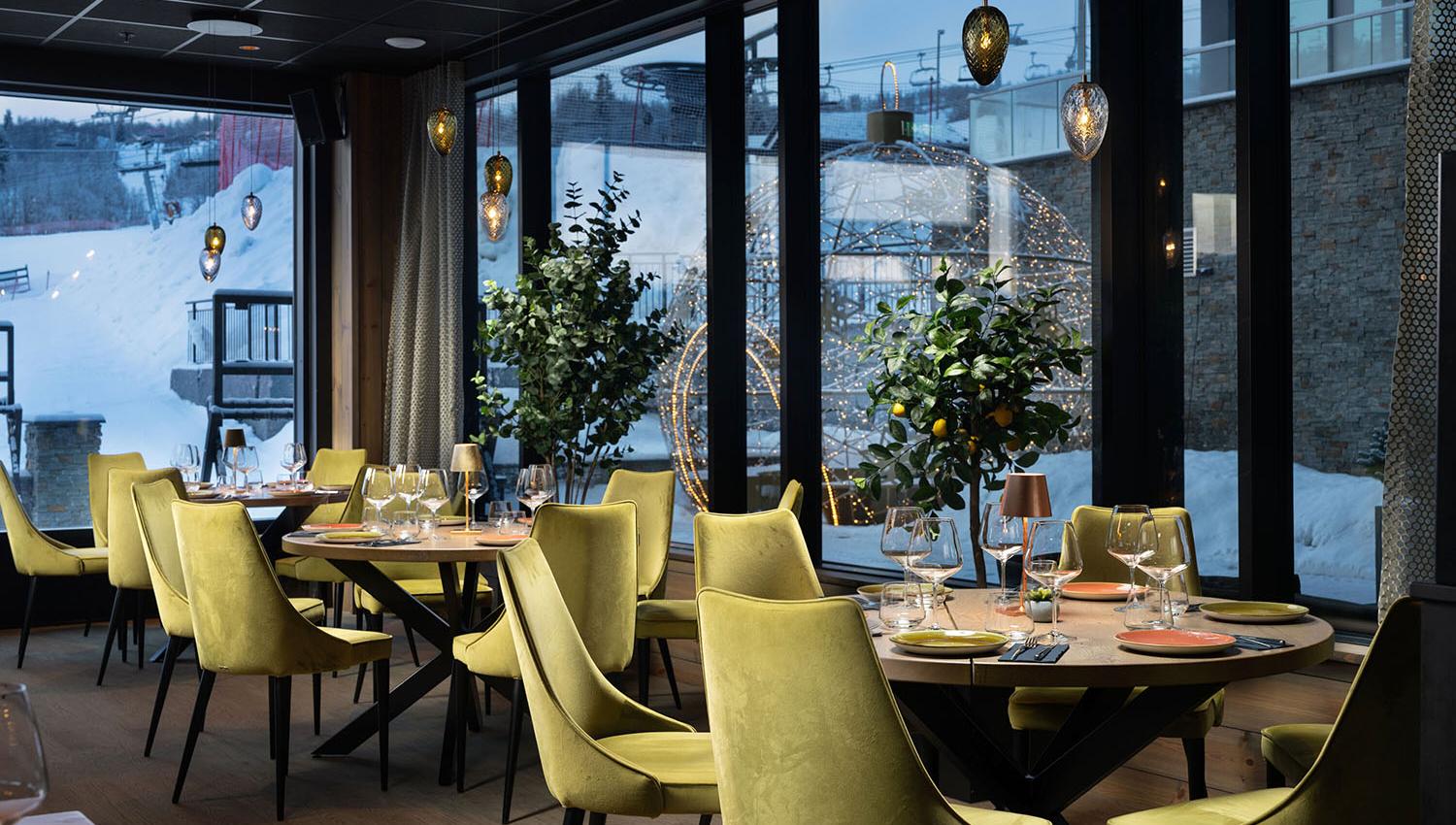 Restaurant interiour with light green cushion chairs and warm lightning. Snow outside.