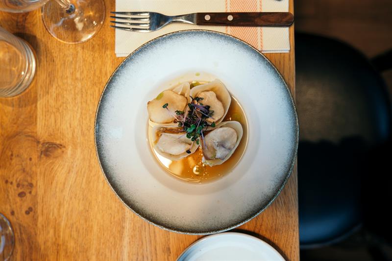 Forrett med delikate dumplings servert i aromatisk kraft og toppet med friske spirer på trebord.