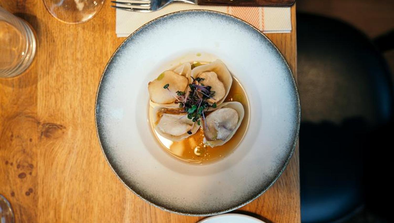 Forrett med delikate dumplings servert i aromatisk kraft og toppet med friske spirer på trebord.