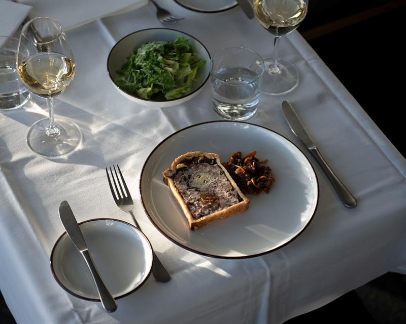 A plate of pâté served with accompaniments on an elegantly set table in natural light.
