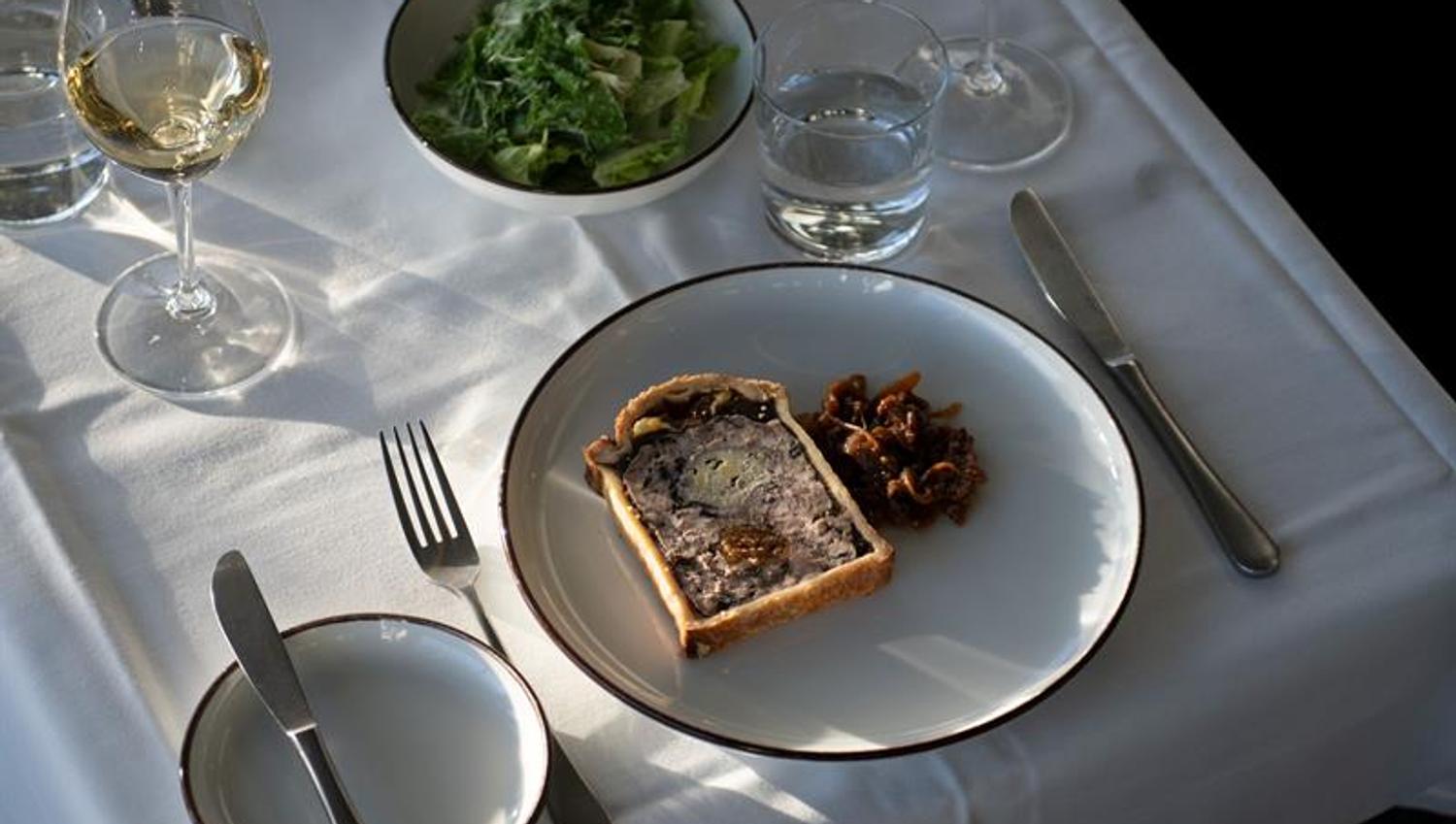 A plate of pâté served with accompaniments on an elegantly set table in natural light.