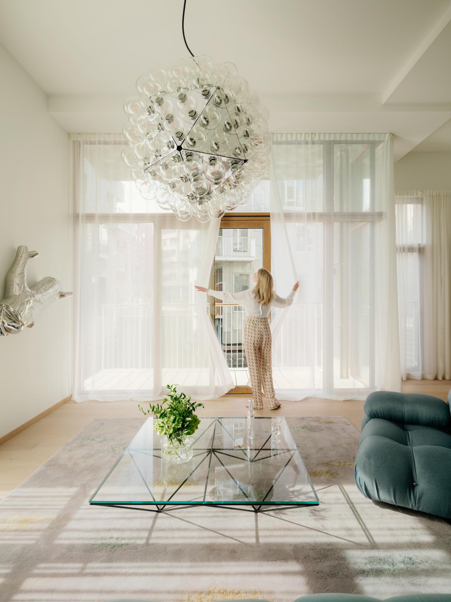 Lady in white living room with large panoramic windows pulling the curtains aside