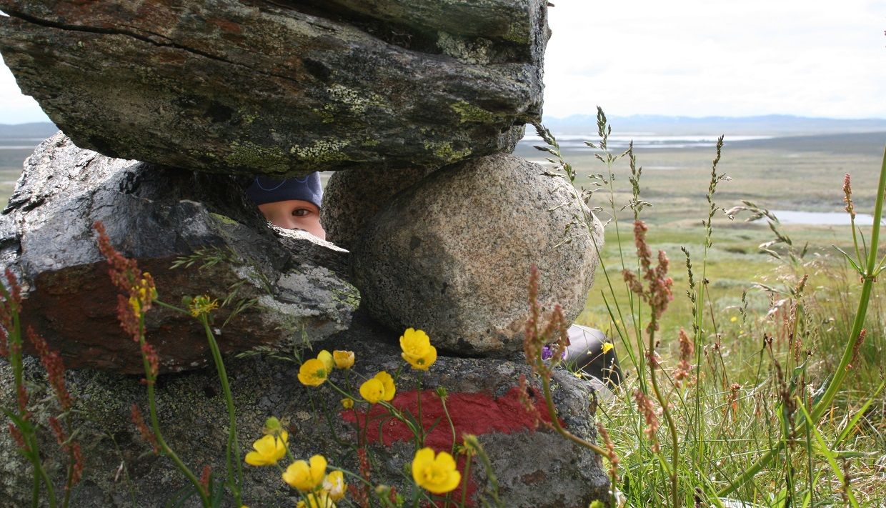 A child peeking through some large rocks in the mountain.