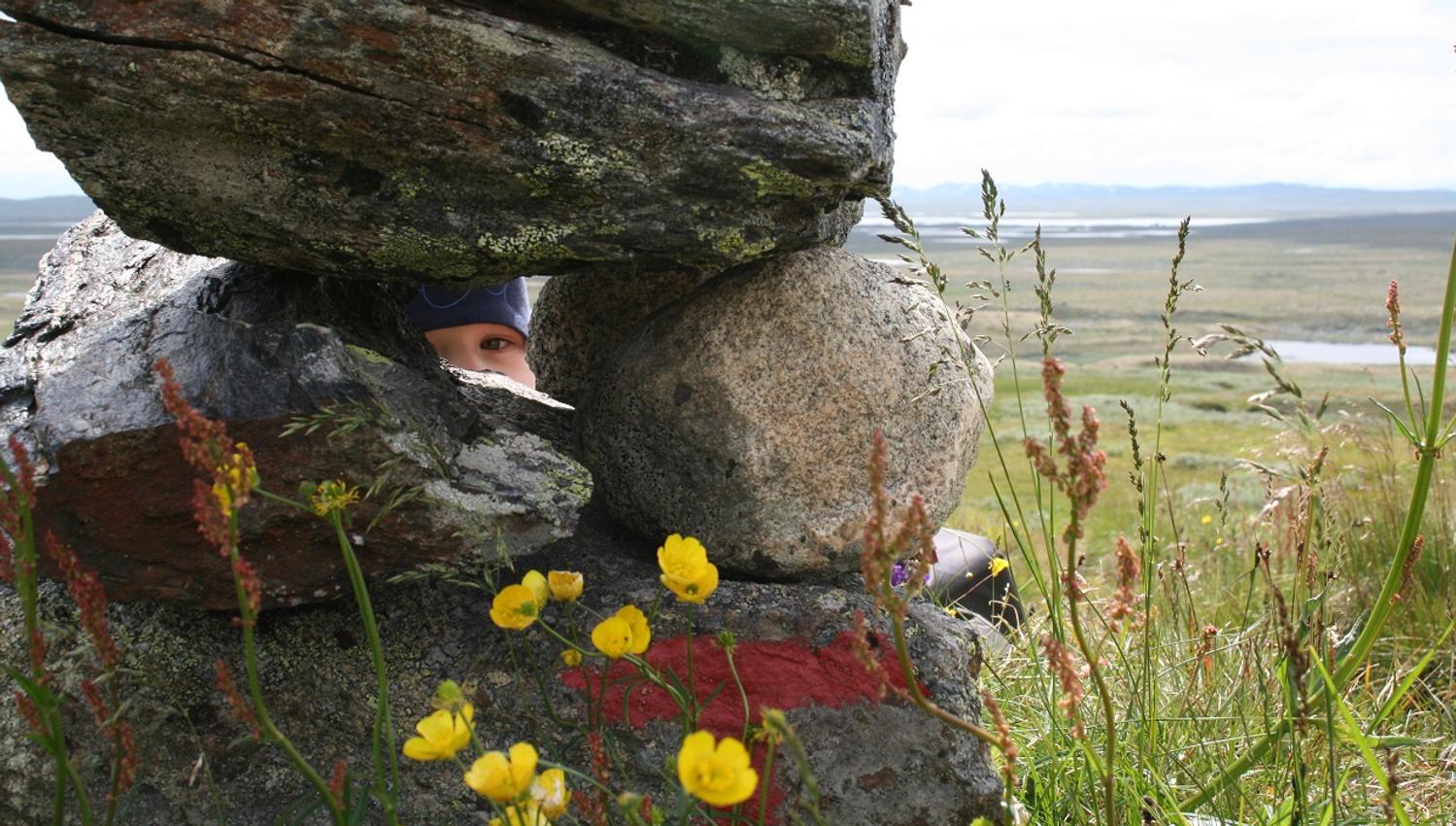 A child peeking through some large rocks in the mountain.