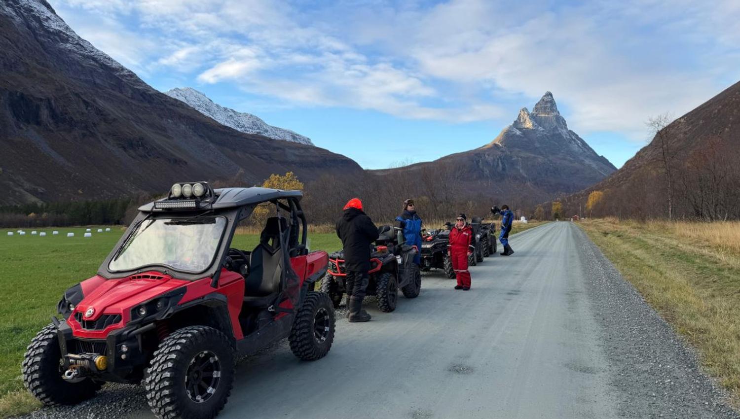 Mange firhjulingen på rekke og rad etter en grusvei. I bakgrunnen kan du se et jorde og høye fjell.
