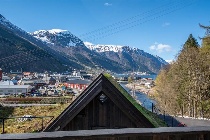Utsikt frå hytte på Lothepus Camping mot Sørfjorden, Odda sentrum og snøkledde fjell i Hardanger på ein klar vårdag