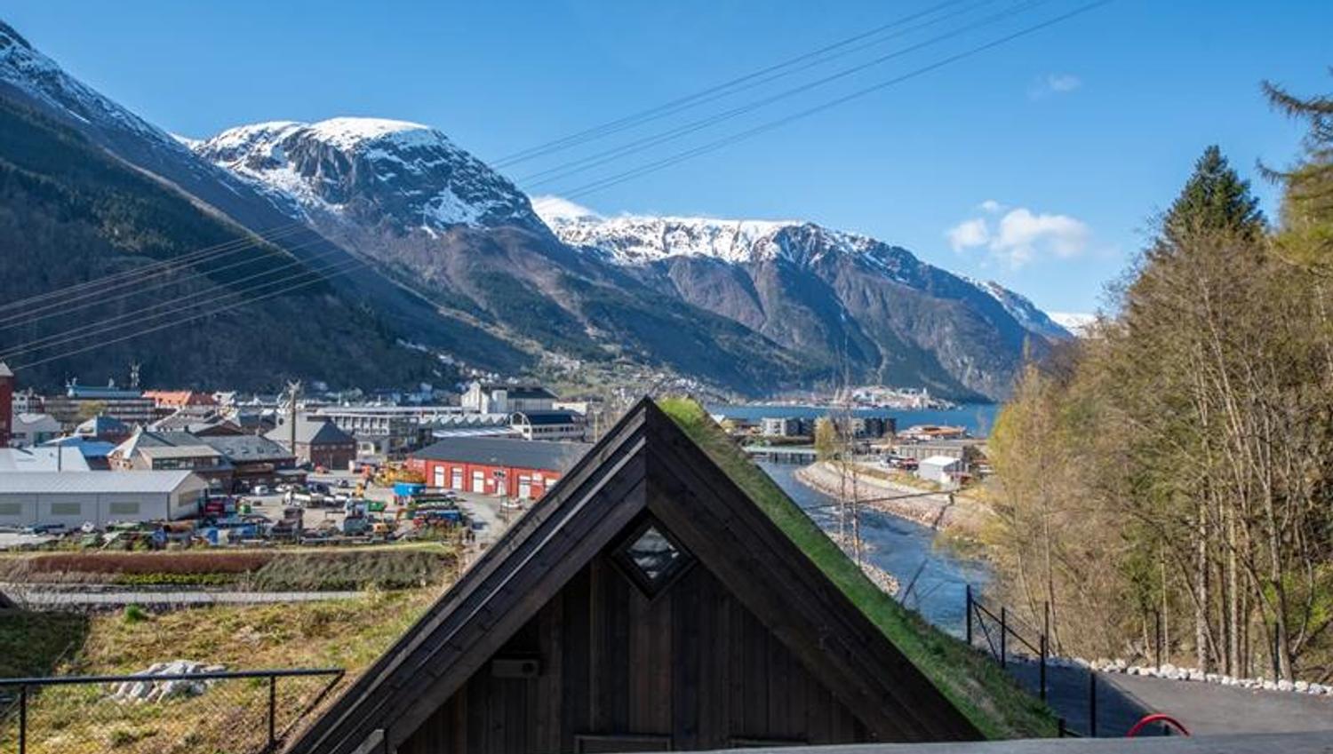 Utsikt frå hytte på Lothepus Camping mot Sørfjorden, Odda sentrum og snøkledde fjell i Hardanger på ein klar vårdag