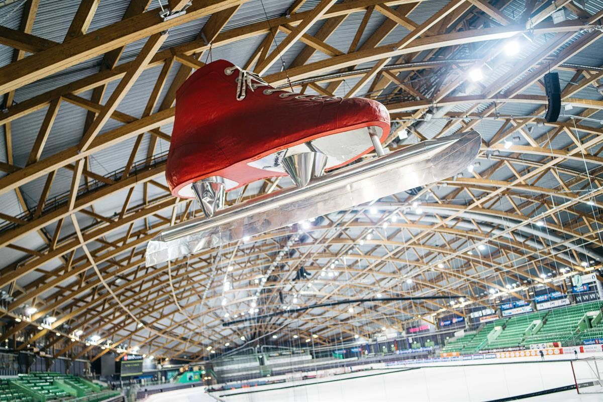 Indoor ice or multi-use arena with a wooden roof structure. A large red skate hangs decoratively above the rink.