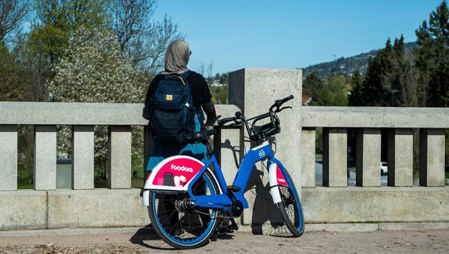 En jente som står ved siden av en bysykkel på en bro og ser mot en åsside