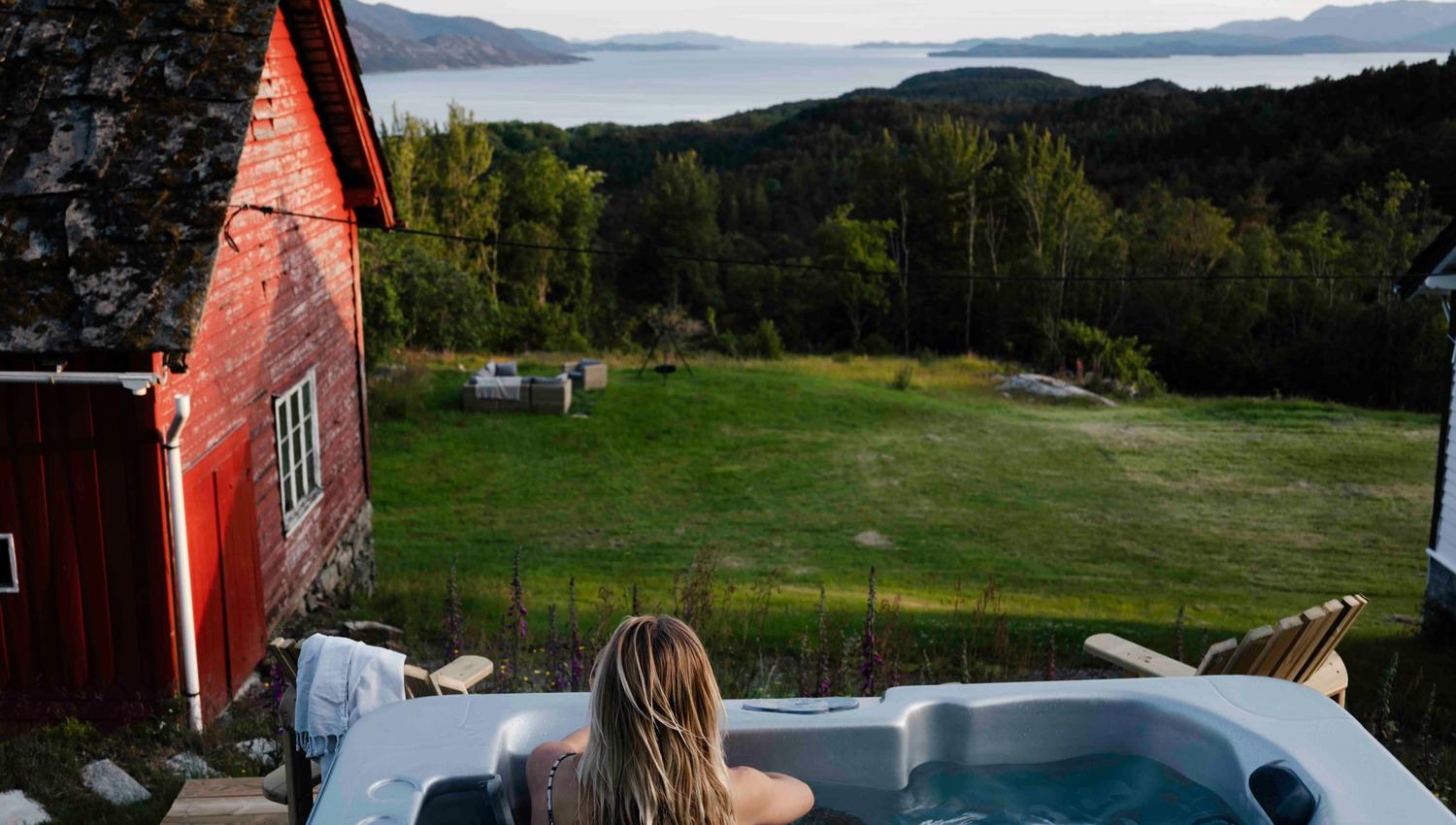 Woman relaxing in the outdoor hot tub overlooking the Hardangerfjord at Stigen Fjordlodge.
