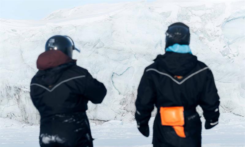 To personer iført snøscooterbekledning, sett bakfra.
