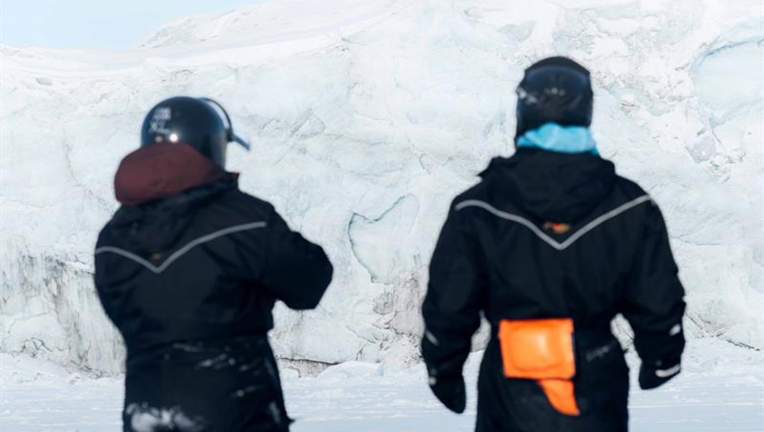 To personer iført snøscooterbekledning, sett bakfra.