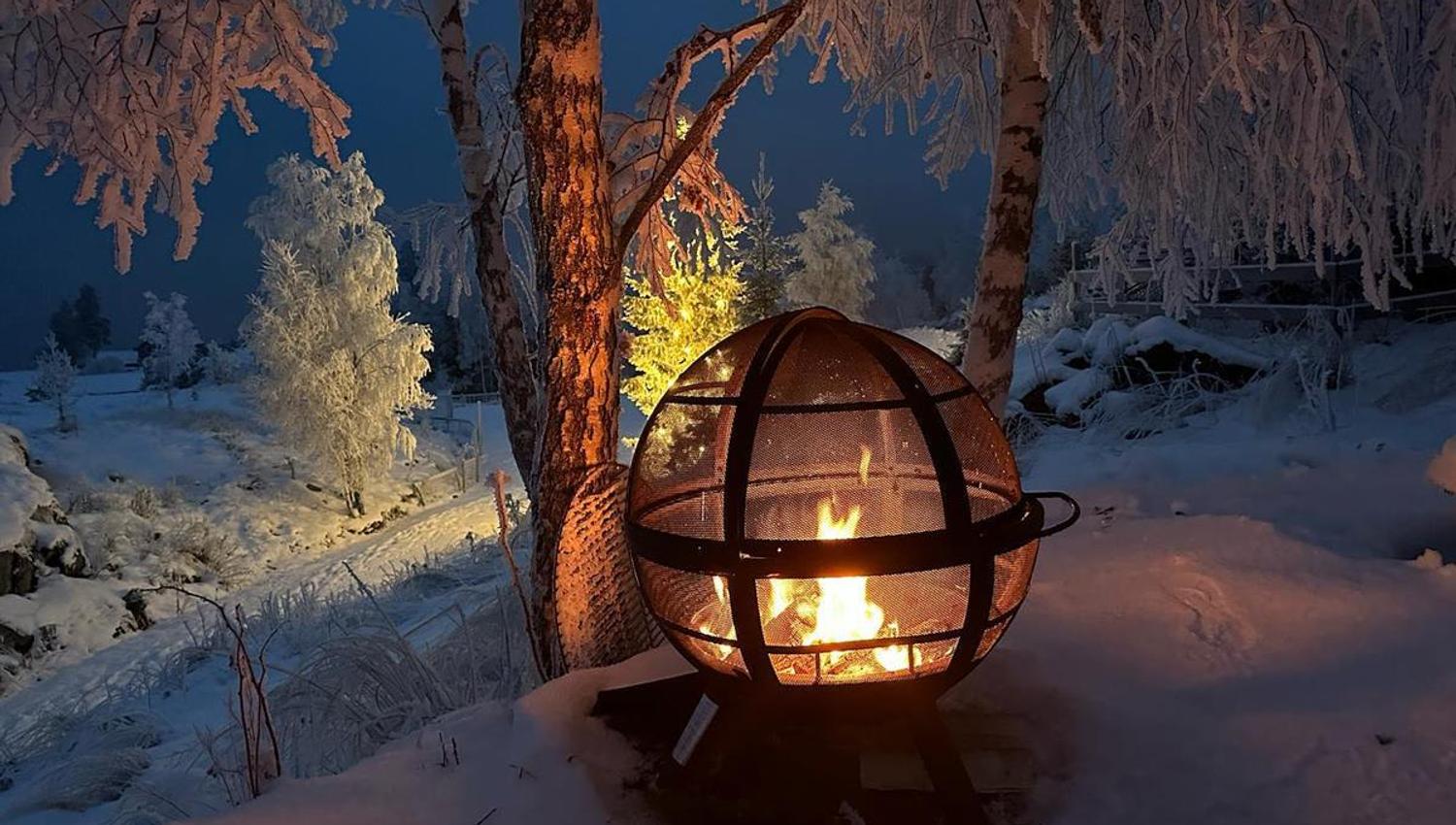 Illuminated fire globe in a winter landscape with snow‑covered trees at dusk.