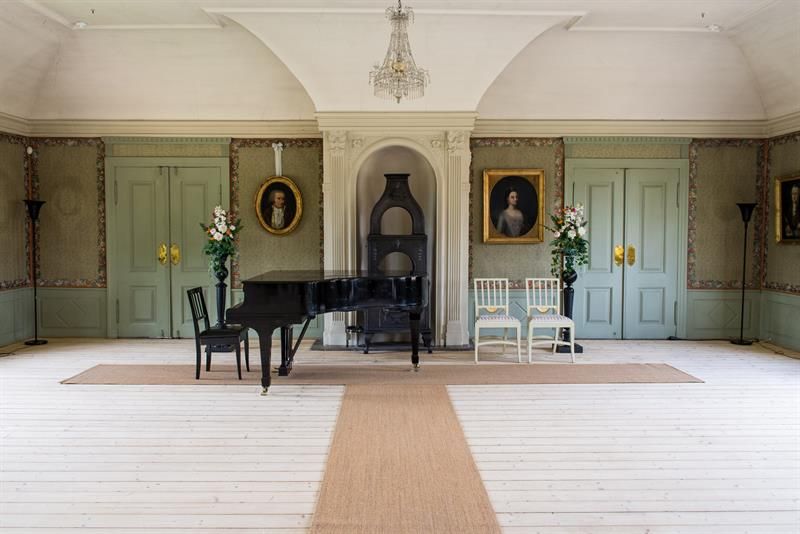 Historic hall featuring a grand piano, portraits and decorative details in a bright and symmetrical room.