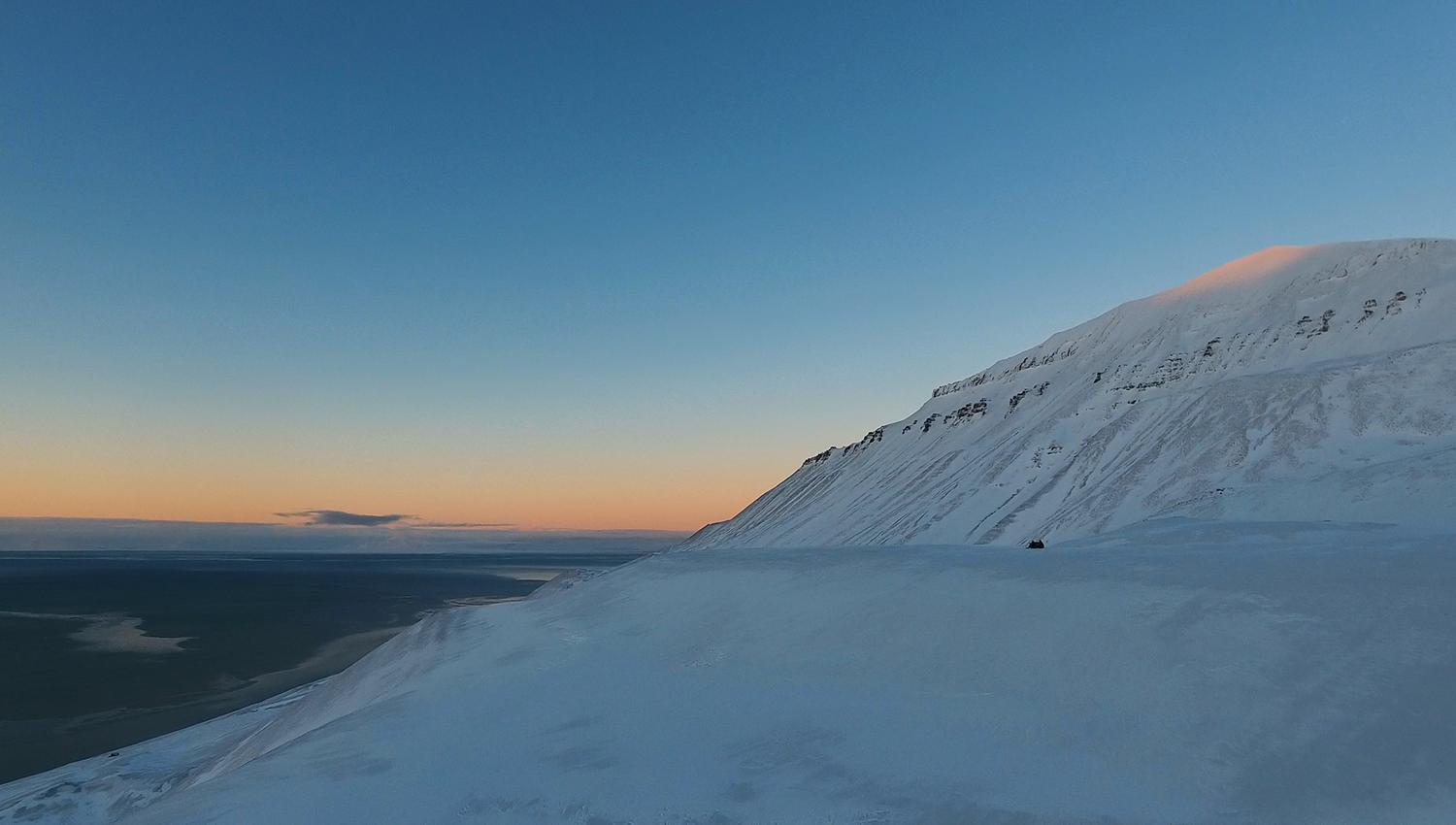 Solstråler fra midnattssola som treffer en fjelltopp