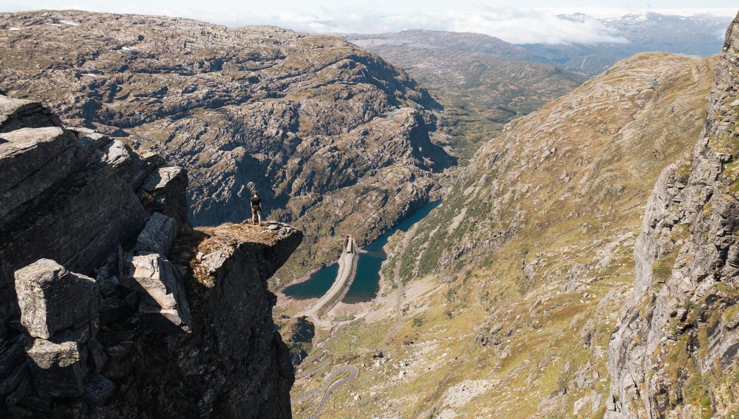Person står på en massiv fjelltopp og ser utover fjellandskapet.