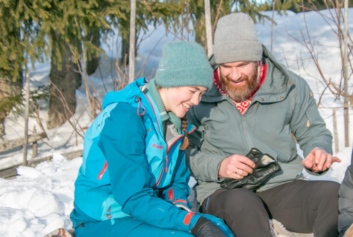 To personer sitter i snøen og ser på en mobiltelefon sammen.