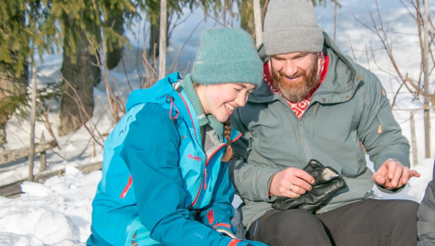 To personer sitter i snøen og ser på en mobiltelefon sammen.