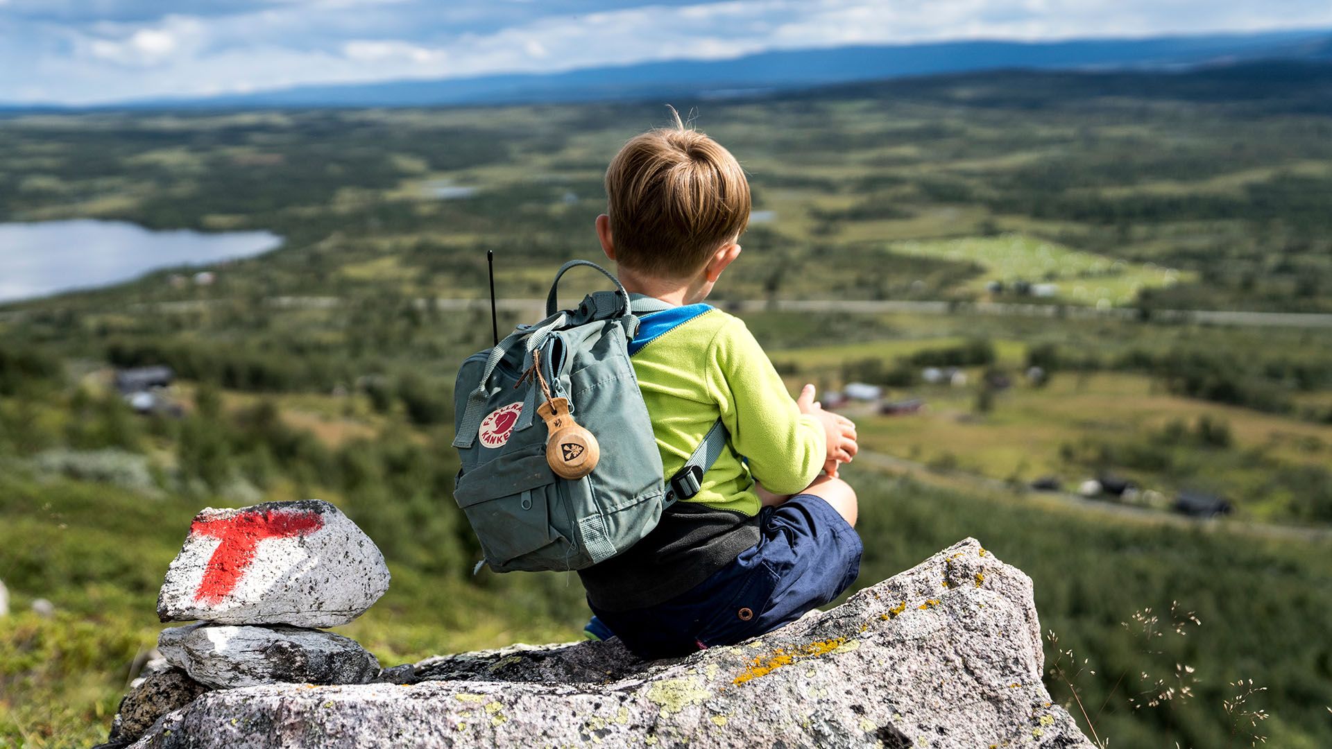 Small kid taking a break on a rock with a painted red T besides him. This indicates that this is along a official DNT path. The view is fantastic.