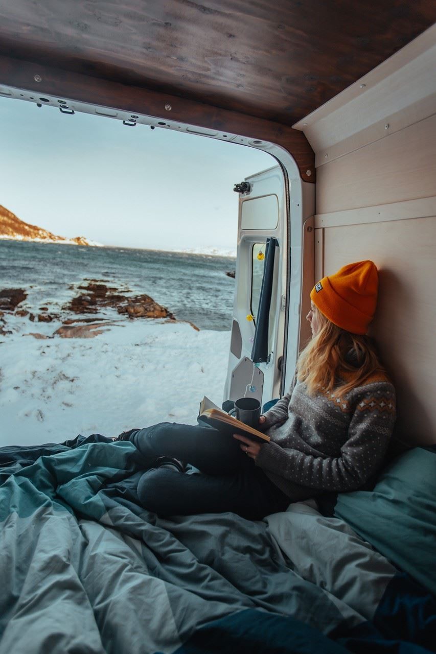 Person sitting in bed inside car looking out