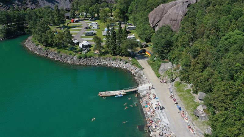 Swimming area at Trolltunga Camping with a pier, bathing guests and the campsite along the water.